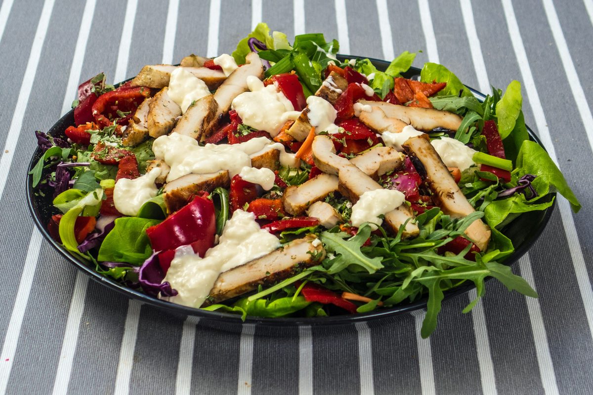 Stor tallerken med kyllingsalat, grønne blader og dressing