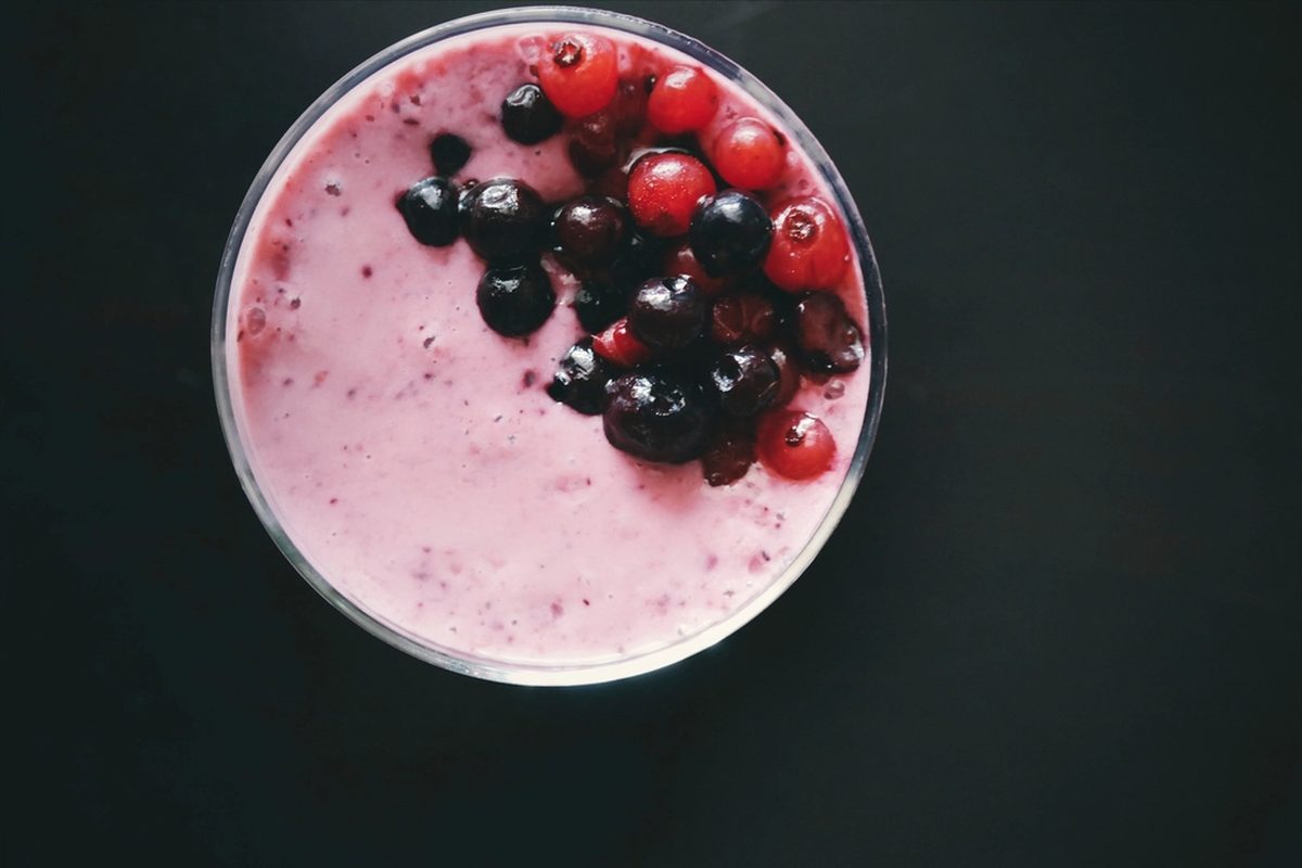 Rosa bærshake i glass med bringebær og blåbær på toppen